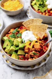 A bowl of turkey chili garnished with sour cream, diced avocado, tortilla chips, and cilantro.